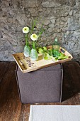 Wooden tray and-decorated with floral pattern on top of square pouffe against stone wall
