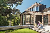 Mother and children on sunny wooden terrace with pergola outside modern wooden house