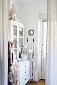White cupboard with glass doors seen through curtains