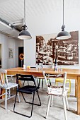 Wooden table, various chairs and black pendant lamps in front of large vintage-style photo
