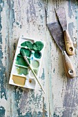 Spatulas, paint brush and artist's palette on wooden surface with peeling paint