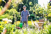 Mann mit Rechen und Gießkanne im Sommergarten