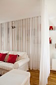 White curtain partition around loose-covered sofa and pouffe