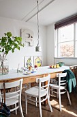 Long table, white wooden chairs and flowering branches in glass vase in dining area