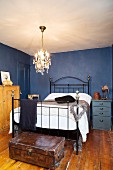 Metal bed in small bedroom with blue walls and old wooden floor