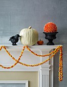 Rabenvogel, Kürbisse, Dekokugel und Girlande aus Candy Corn als Halloweendekoration auf Kaminsims