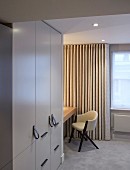 Fitted wardrobe with leather strap handles and chair in front of floor-length curtains on window
