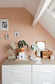 Ornaments on top of chest of drawers against salmon-pink wall