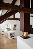Restored roof beams and open fireplace below suspended chimney in elegant white attic bedroom