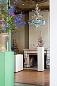 Glass artworks on white plinths, coloured glass chandelier and flowers in antique interior