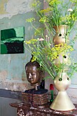 Fennel flowers in artistic vase next to head of Buddha in vintage interior