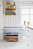 Grey wooden bench, wooden crate on castors and retro tins on wall-mounted shelves in white-tiled kitchen