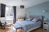Bedroom with pastel-blue accent wall and grey upholstered headboard