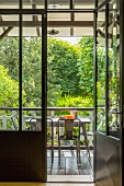 Open door leading to table and chairs in loggia with view of garden