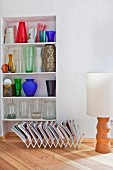 Colourful glass vases on shelves in niche behind magazine rack and floor lamp