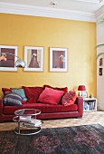 Scatter cushions on red sofa below pictures on yellow wall and side table on rug in period apartment