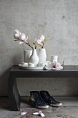 Magnolia flowers in white vases on wooden bench against concrete wall