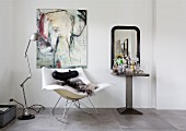 Animal-skin blanket on designer rocking chair below picture of elephant, industrial-style standard lamp and drinks table