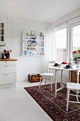 Dining table on Oriental rug in white country-house kitchen