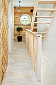Pale wooden staircase and rustic wood-clad walls in renovated period building with bulls-eye window