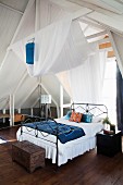 White fabric draped over roof structure above metal bed in airy bedroom