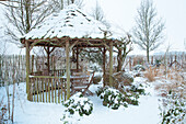 Wooden pavilion with snow-covered roof in winter garden