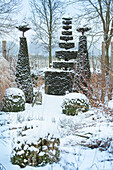 Winterlicher Garten mit schneebedeckten Formschnitt-Bäumen