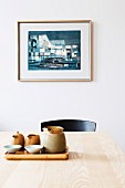 Still-life arrangement of tray and ceramics on wooden table in front of framed picture