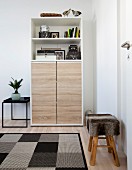 Stool with fur cover and geometric rug in front of cabinet with oak doors below open shelves