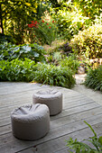 Zwei Sitzpoufs auf runder Holzterrasse im Sommergarten