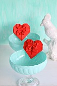 Red origami hearts in turquoise dessert bowls next to china bird