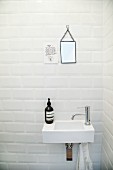 Waschbecken und kleiner Wandspiegel neben Spruch an weißer Fliesenwand