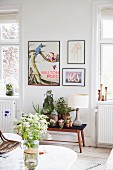 Vase of white wildflowers on marble coffee table and plant stand below black-framed pictures on wall in living area