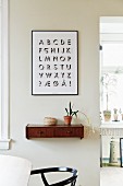 Graphic alphabet artwork above wooden wall-mounted shelf