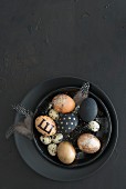 Black and gold Easter eggs, feathers and quail eggs in black bowl