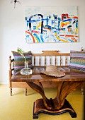 Art-Deco table in front of bench with turned spindles below modern artwork on wall