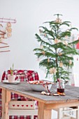 Jar of honey, dried apple slices, bowl and cups on wooden table in front of small Christmas tree with straw stars