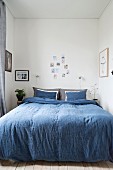 Blue bed linen on double bed and various photos decorating walls of narrow bedroom