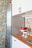 White kitchen counter with unrendered brick splashback next to floral wallpaper