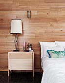 Bett und schlichter Nachttisch vor einer mit Holz verkleideten Wand