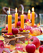 Orange Kerzen in Tontöpfen, dekoriert mit Malus (Äpfel, Zieräpfel)
