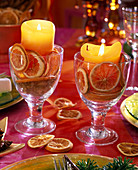 Gläser mit Fuß mit gelben Kerzen, gefüllt mit Orangenscheiben