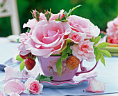 Blüten von Rosa (Rosen), Fragaria (Erdbeeren) in Kaffeetasse, Blütenblätter