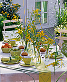 Tischdekoration mit Solidago (Goldrute), Gräsern, gelbem Peddigrohr, Gedecke