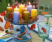 Hagebutten, Herbstlaub von Prunus (Kirsche), Kerzen auf Glas - Schale