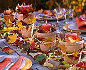Leaves and apple as table decorations in candlesticks made of terracotta pots
