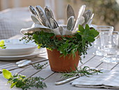 Herbs around clay pot with cutlery wreath