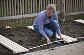 Woman measuring distances of wooden grates in flower beds