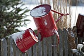 Red watering can and bucket with snow, turned over on garden fence