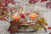 Kleine Gläser mit Kerzen als Windlichter auf Birkenscheibe, dekoriert mit Ranke